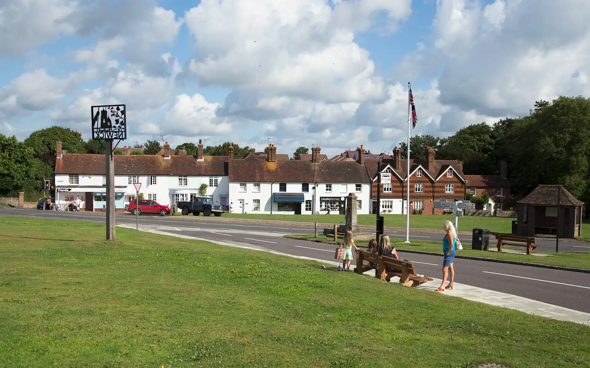 A view of Newick village green, with people sat waiting at the bus stop.