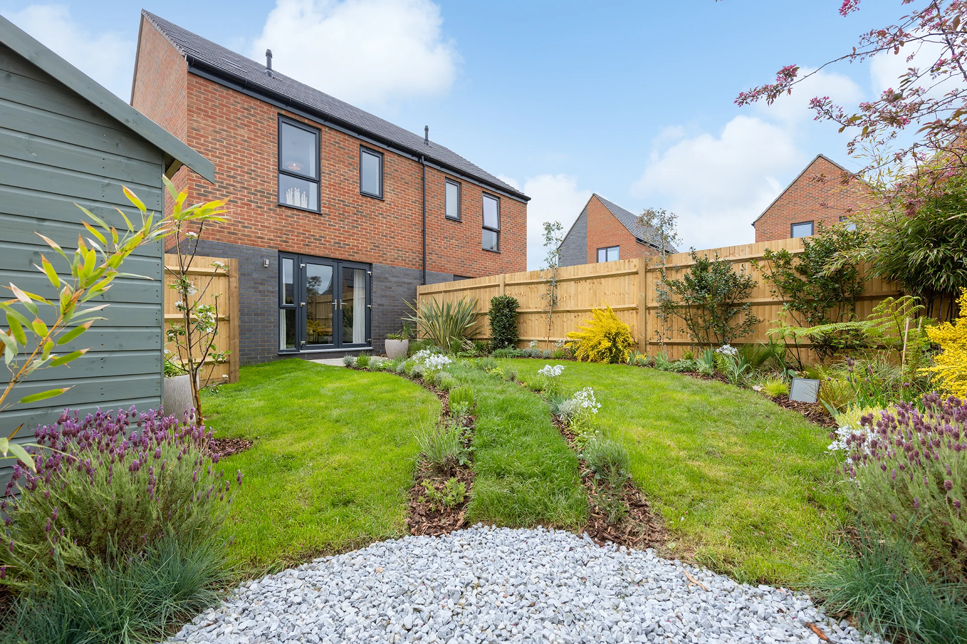 A view ofa biodiverse garden looking towards the rear of a house. a hed is seen off to the left.